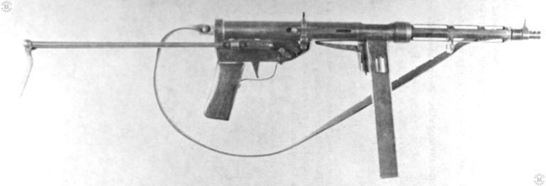 The TZ-45 submachinegun, produced in Italy the last year of WWII. This design is fairly straightforward, though the weapon was roughly made and finished. On the rear of the magazine well can be seen one of the innovations of this weapon, a grip safety. The TZ-45 was possibly the first weapon to actively included this feature. The operator holds the magazine well with his non-firing hand and squeezes in the short leg of the “L” shaped safety. That squeezing causes the rear, long leg, of the safety to disengage the bolt, allowing it to travel forward and the weapon to fire. There is also a mechanical safety switch located just above the front of the trigger guard. The long sliding stock’s legs are able to enter the two holes in the lug found under the middle of the barrel jacket. PHOTO CREDIT: US Army