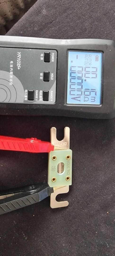 A CNL Fibre Glass Fuse is shown with a digital measuring device reading 68068 beside a small metallic tool featuring a greenish base and red/black handles, all set on a dark fabric surface.