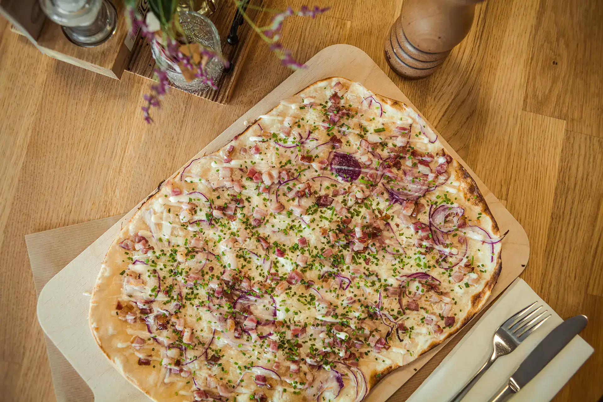 Flammkuchen mit Speck und Zwiebeln auf Holzbrett