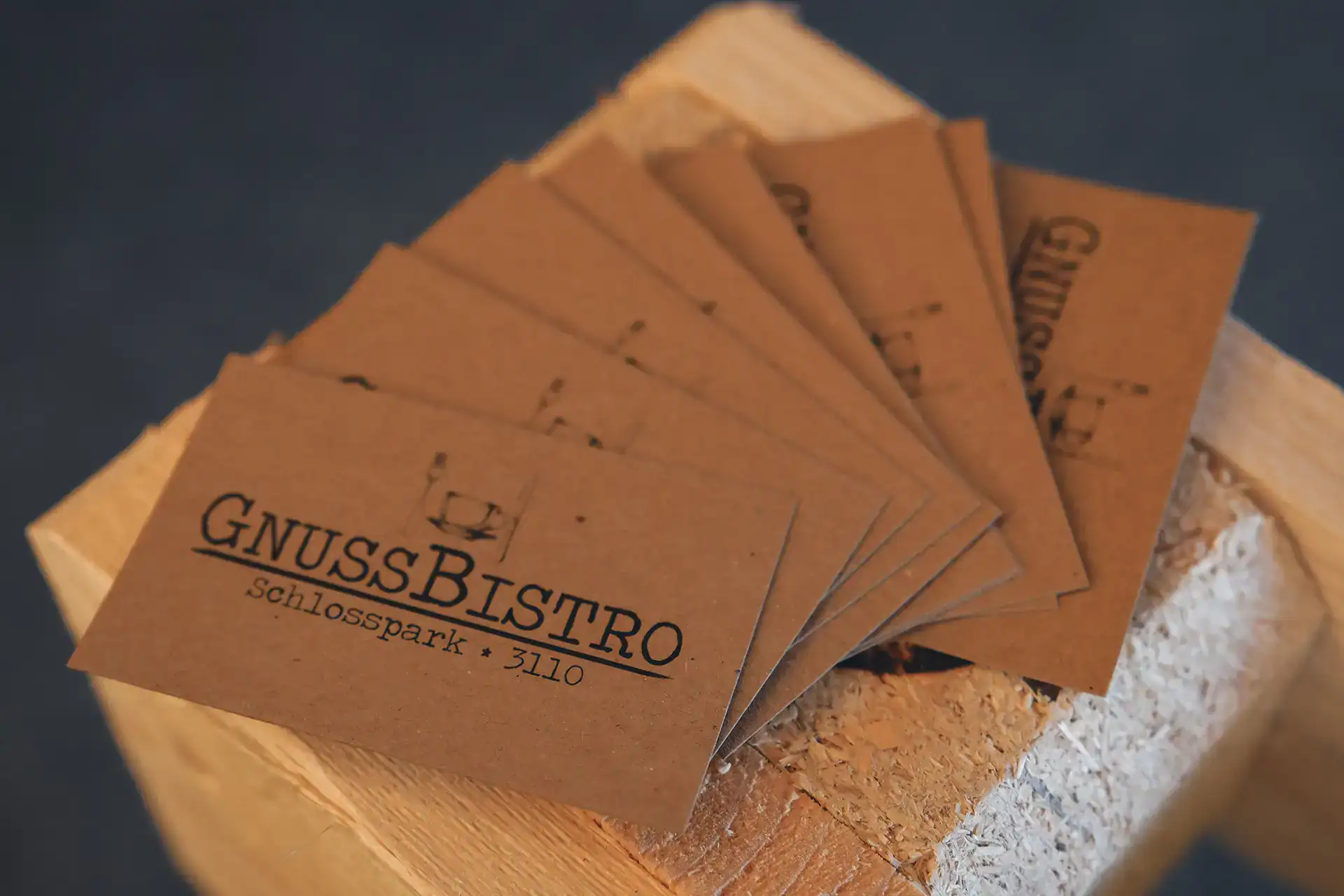 Mehrere Visitenkarten mit GnussBistro Logo auf Holzuntergrund