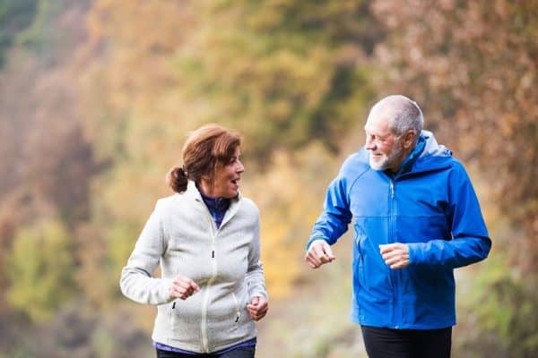 Beautiful active senior couple running together outside in sunny autumn nature