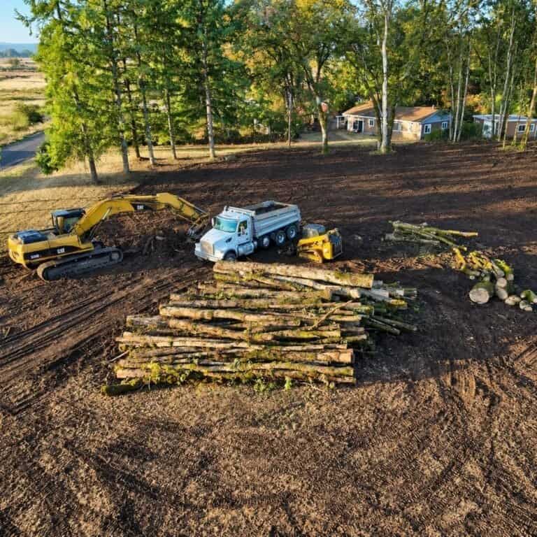 Cleared lot with stacked logs and an excavator after land clearing in Hillsboro, Oregon