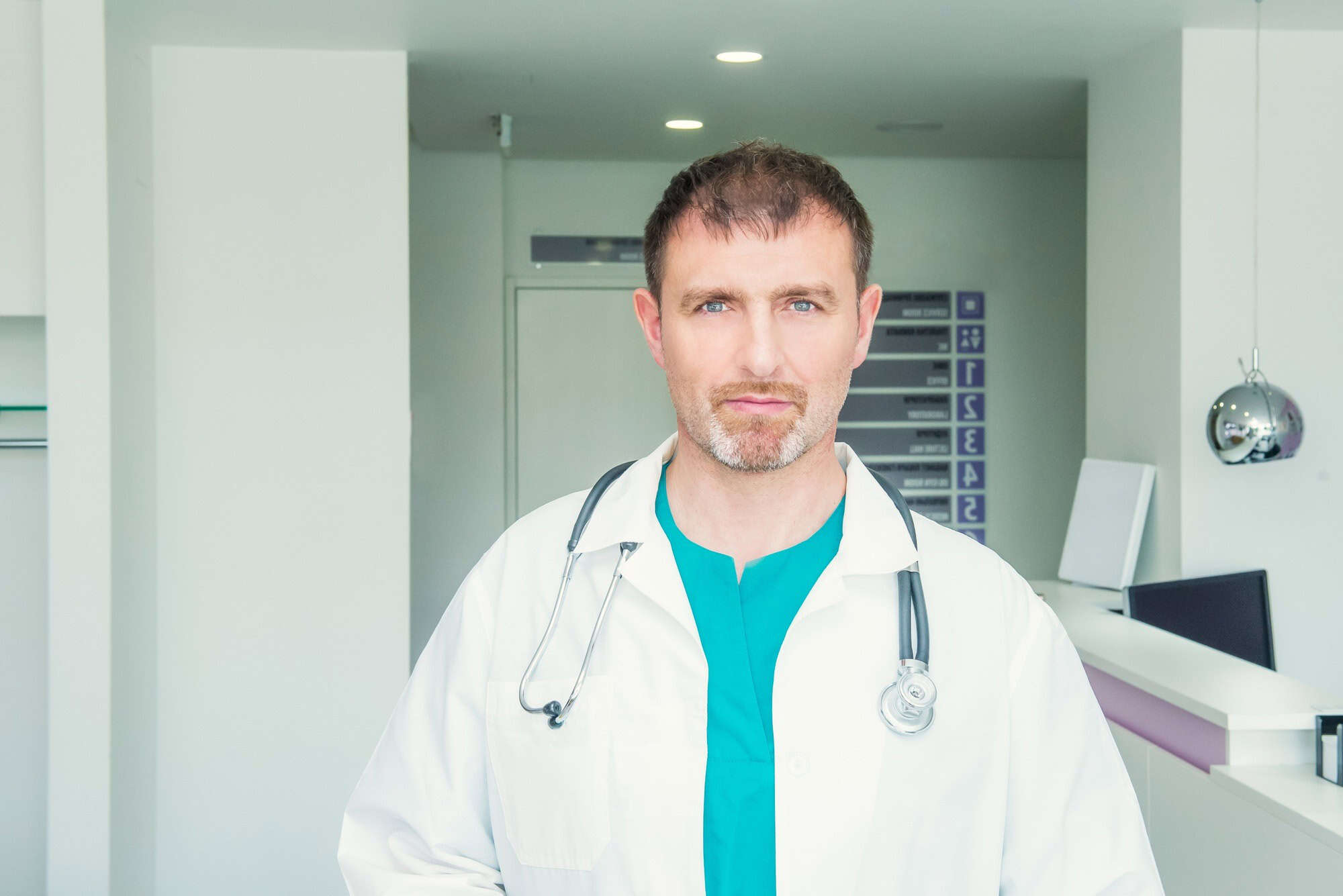 Mature male confident Doctor's portrait standing in the hall of the modern medical clinic.