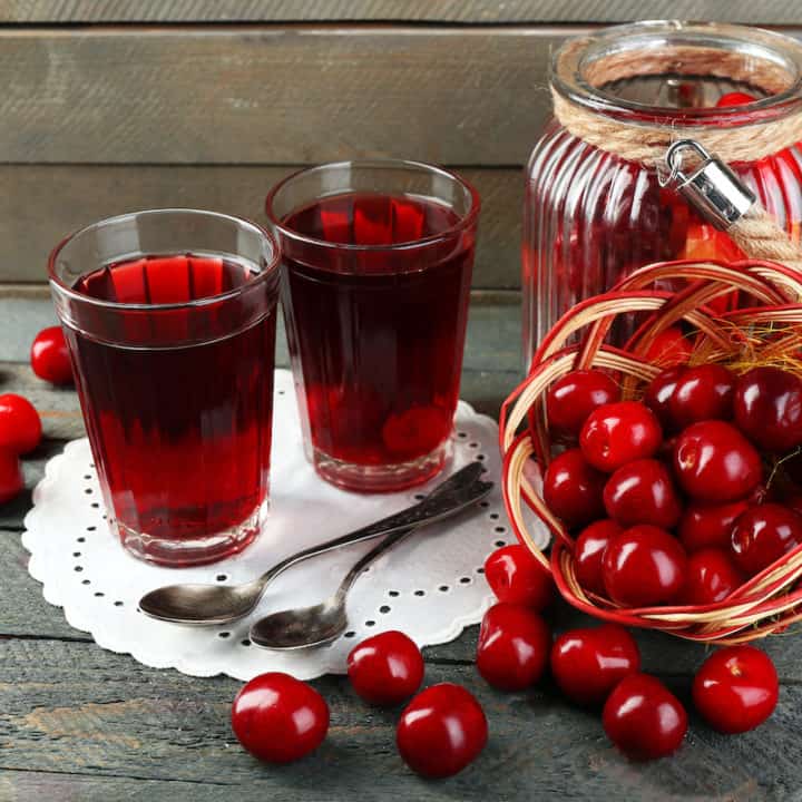 glasses of cherry kompot next to fresh cherries.