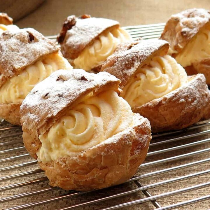 A group of Polish cream puffs, also known as Ptysie, delicately arranged on a cooling rack and dusted with powdered sugar.