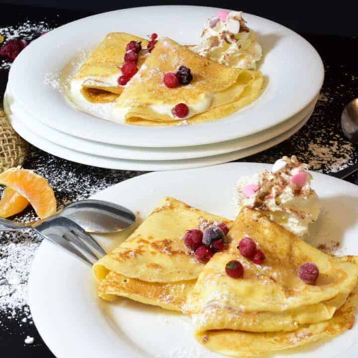 Two plates with delicious Polish crepes and ice cream on them.