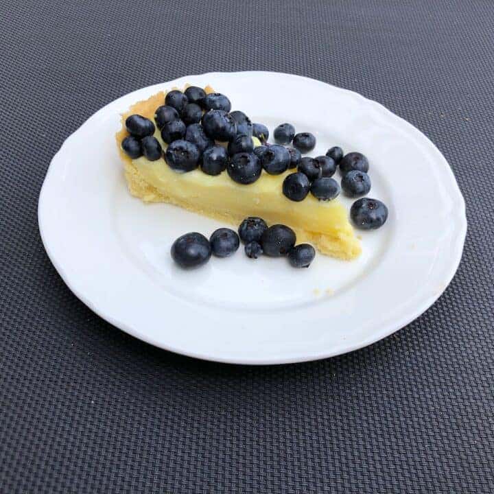 A lemon tart topped with blueberries on a white plate.