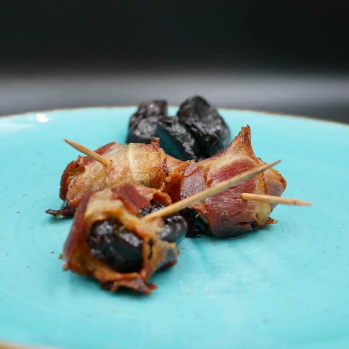 Bacon wrapped prunes on a blue plate.