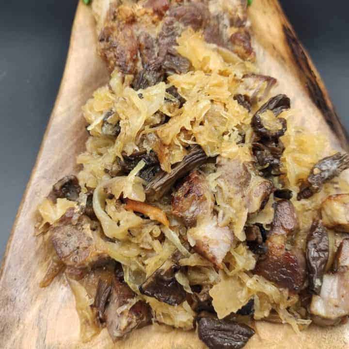 Bigos Myśliwski, a traditional Polish Hunter's Stew Recipe, featuring sauerkraut and meat on a wooden cutting board.