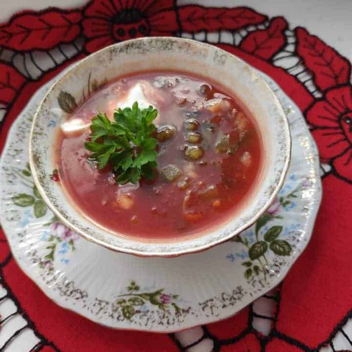 A bowl of Chłodnik Pomidorowy, a Polish cold tomato soup, on a red tablecloth.