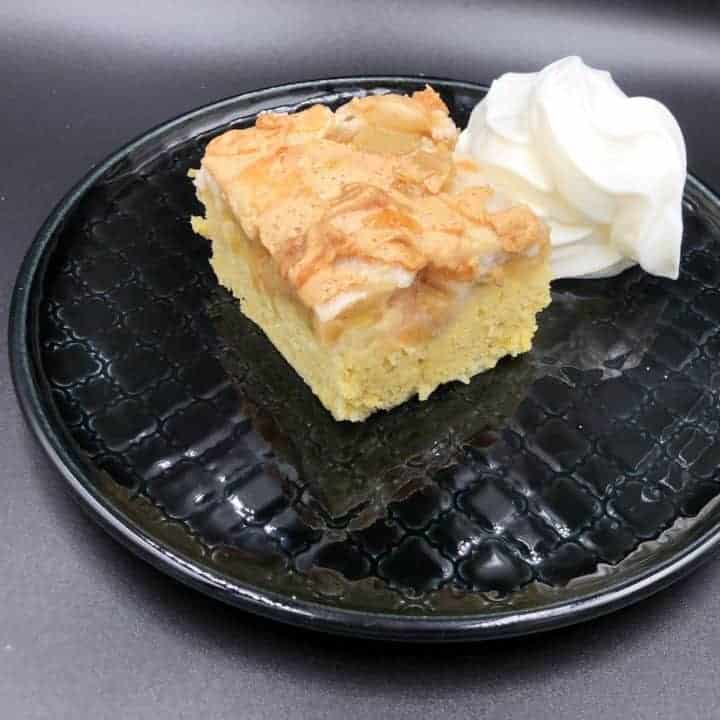 A delicious Polish Rhubarb Cake Recipe served on a black plate with a dollop of whipped cream.