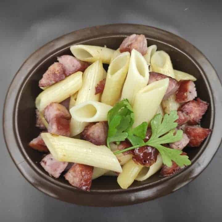 A bowl of Polish sausage pasta garnished with parsley.