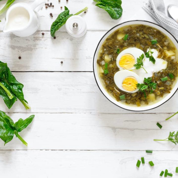 A bowl of Polish sorrel soup with spinach and eggs on a white table.