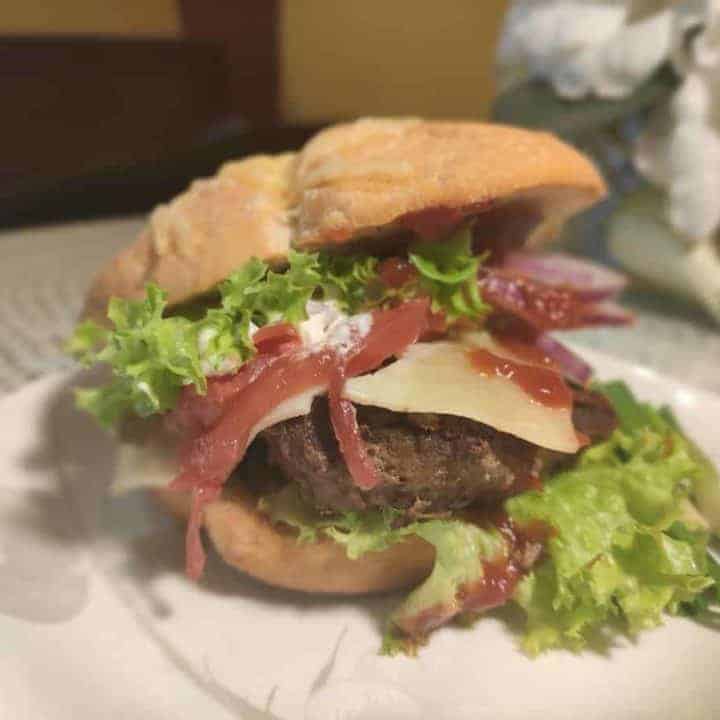 A Polish hamburger recipe served on a plate with lettuce and bacon.