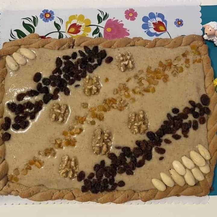 A Polish Easter mazurek cake adorned with nuts and eggs is displayed on a table.