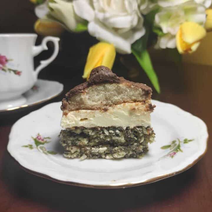 A piece of cake on a plate next to a cup of tea.