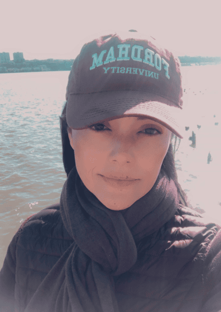 Shenae, wearing a baseball cap from her alma mater Fordham University, standing in front of a body of water