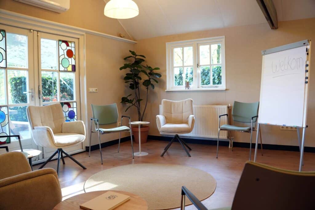 Training opstelling met comfortabele stoelen, een kleed en een flipover bord in een warme ruimte bij vergaderlocatie Ruimte voor Inzicht in Oisterwijk