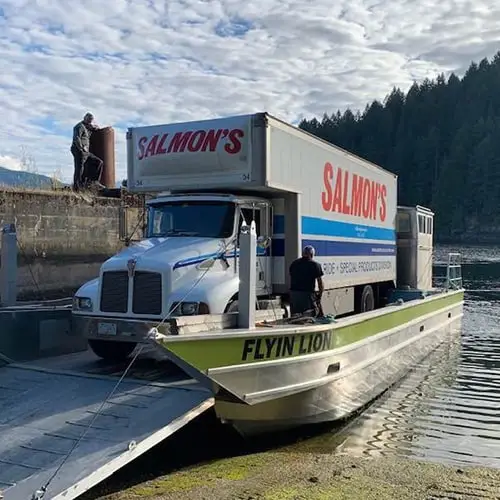 Salmon's moving truck being transported on Flyin Lion ferry boat across water with forested mountains in background