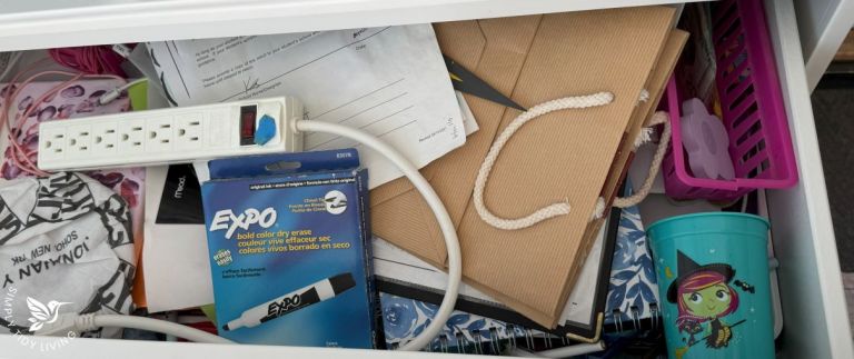 A cluttered junk drawer with scattered papers, tangled cords, a power strip, and miscellaneous items.