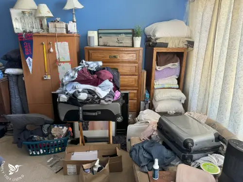 A cluttered bedroom with piles of clothes, scattered boxes, and an overstuffed suitcase, showing the starting point before decluttering.