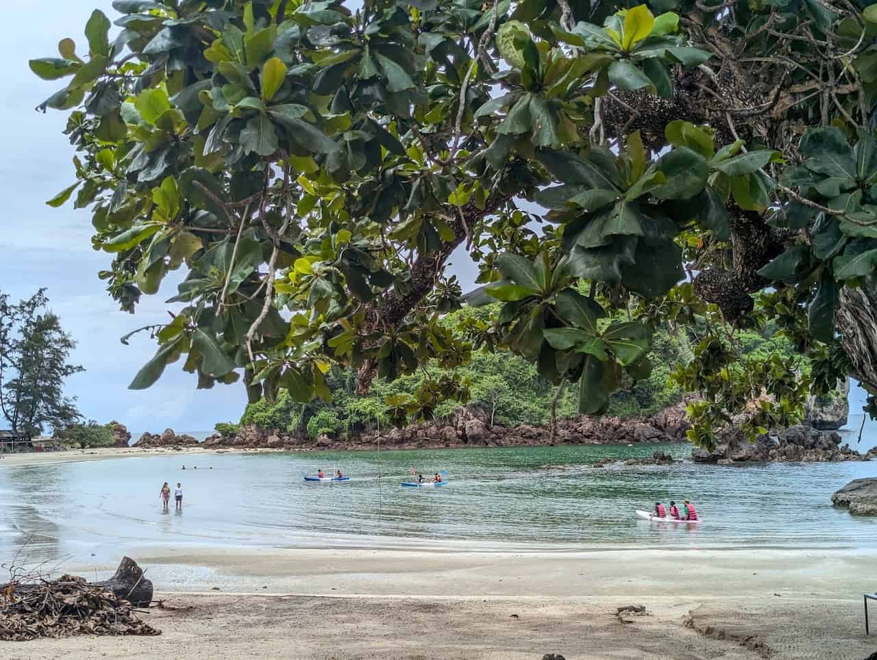 Cyclists riding along the scenic coastline near Krabi, passing limestone cliffs, tropical beaches, palm trees, and peaceful coastal roads during a Thailand cycling adventure.