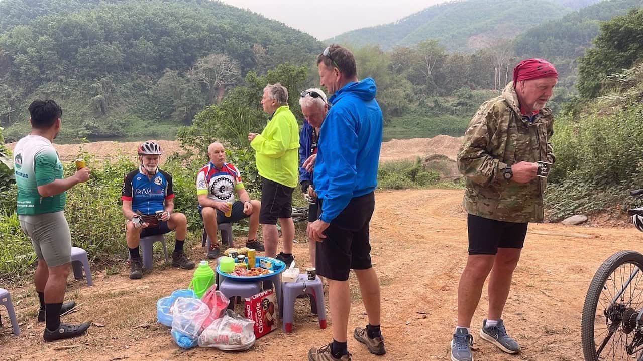 Cyclists taking a refreshment break during a northern Laos backroad cycling adventure, surrounded by mountain scenery, rural villages, and peaceful countryside landscapes.