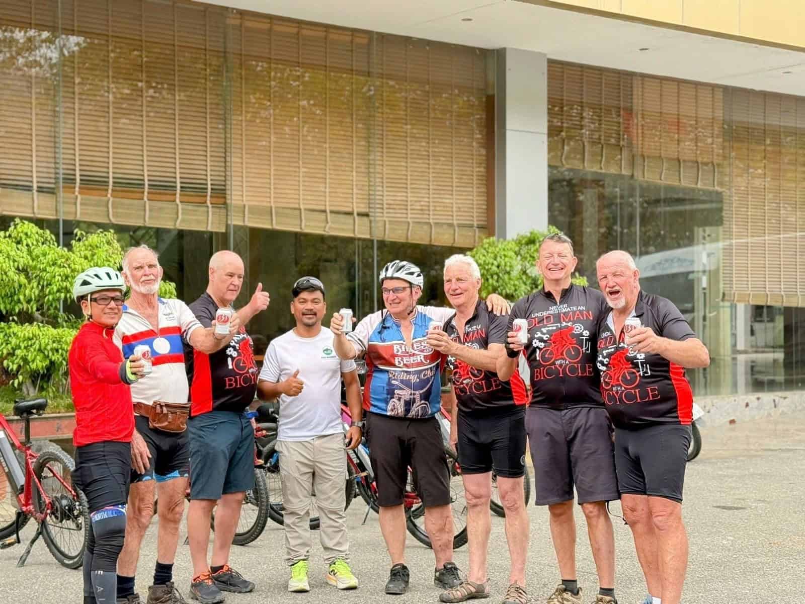 Cyclists riding from Thailand to Laos on scenic backroads, passing rural villages, mountain landscapes, riverside roads, and cultural landmarks on a cross-border cycling adventure.
