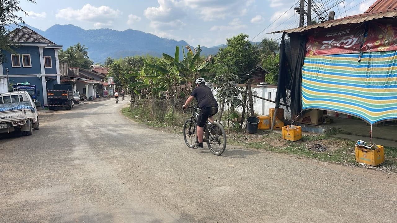 Cyclists riding along a peaceful countryside route near Vientiane, Laos, passing rice fields, rural villages, and scenic backroads on a journey to Luang Prabang.