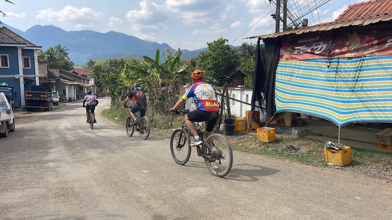 Cyclists riding from Vientiane to Luang Prabang on scenic backroads through rural Laos, passing traditional villages, mountain landscapes, and peaceful countryside routes.