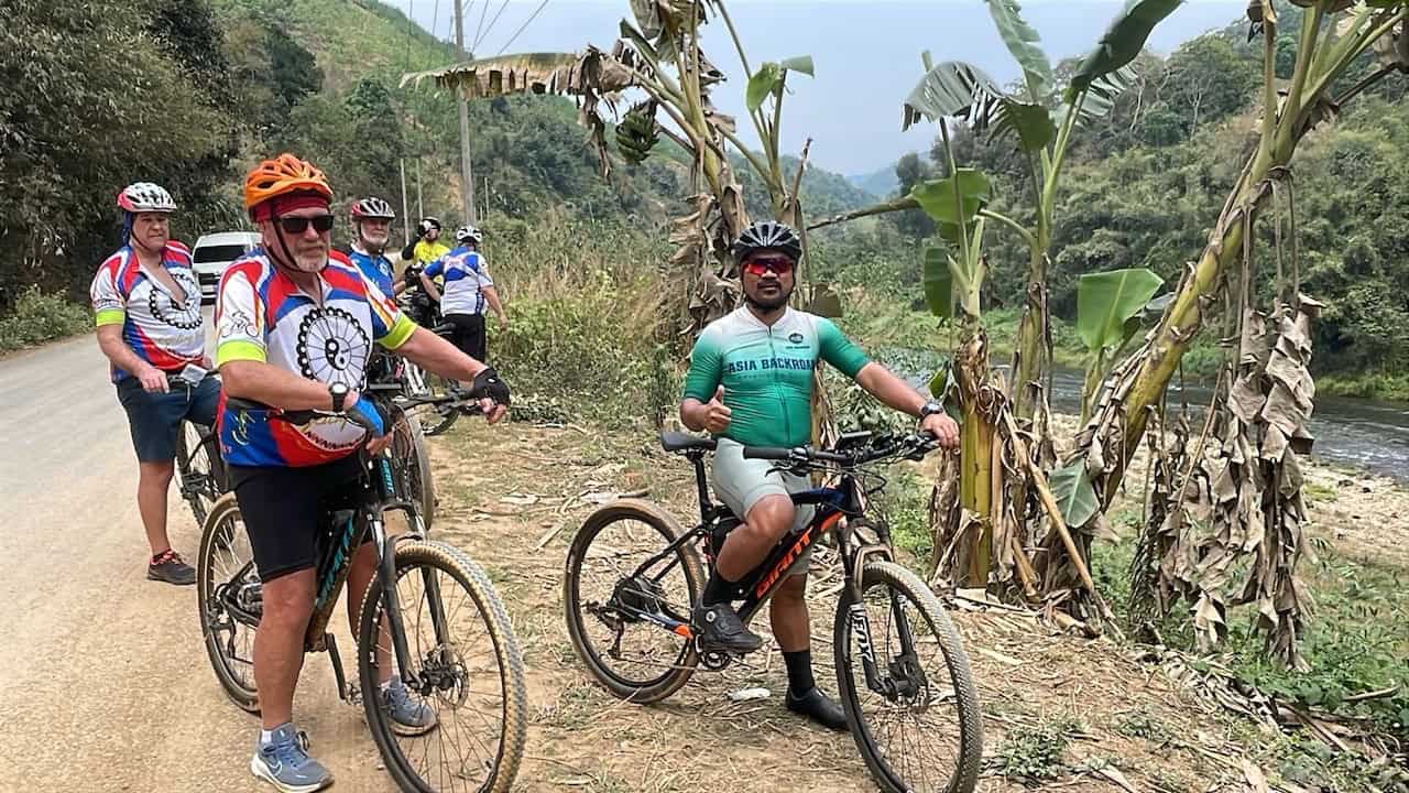 Cyclists riding through the remote mountains and rural backroads of northern Laos, surrounded by lush landscapes and traditional villages on an Indochina cycling tour.