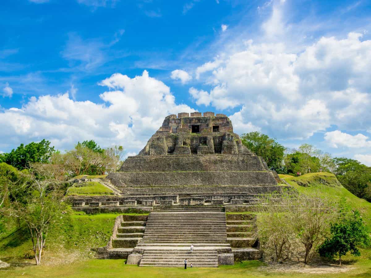 Mayan ruins of Xunantunich in Belize. Mayan Ruins of Xunantunich in Belize. Stone pyramid surrounded by green grass, with blue sky and white clouds in the background.