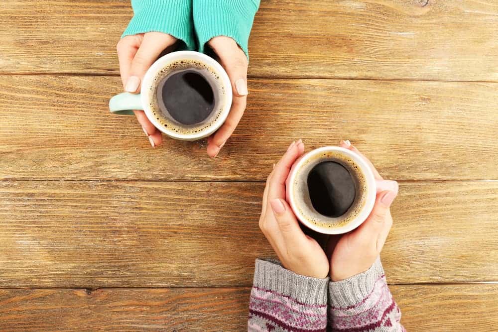 Two people holding cups of coffee at a wooden table