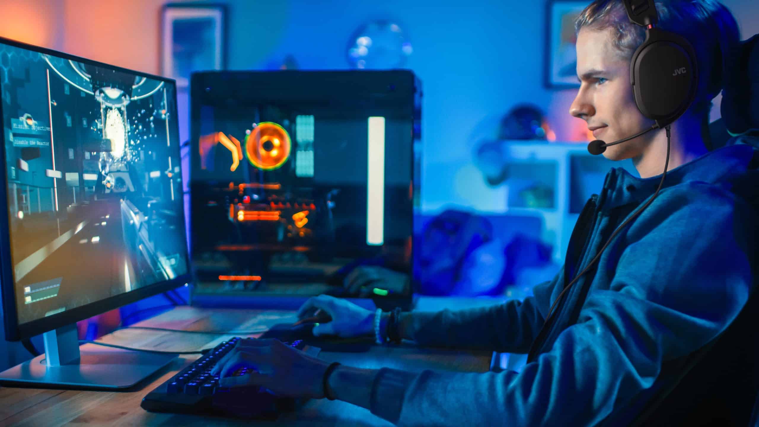 Cheerful Gamer Playing First-Person Shooter Online Video Game on His Powerful Personal Computer. Room and PC have Colorful Neon Led Lights. Cozy Evening at Home.