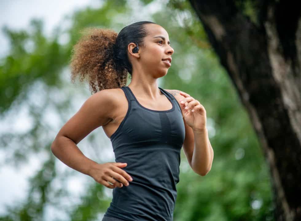 A woman of African descent is jogging through a forest. She is wearing athletic clothing.