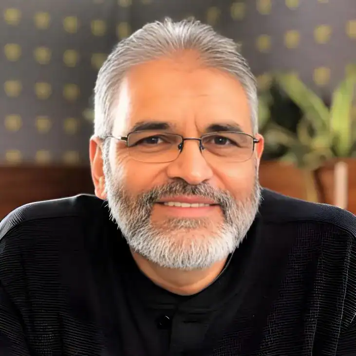 Afzul Soobedaar, founder and director of Perispec Consulting, smiling confidently in a black shirt with glasses and grey hair and beard, seated in a warm, professional setting. Afzul is an experienced strategy consultant and workshop facilitator based in South Africa.
