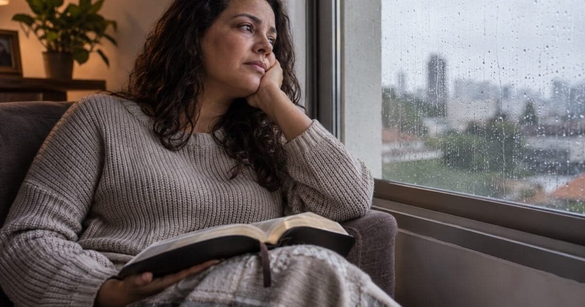 Mulher com uma Bíblia aberta no colo observa a chuva pela janela, ilustrando a espera e a oração no Salmo 13.