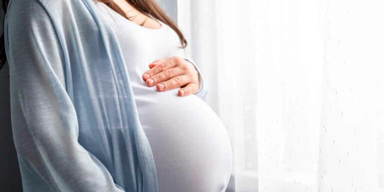 Gestante com a mão apoiada sobre a barriga durante a gravidez