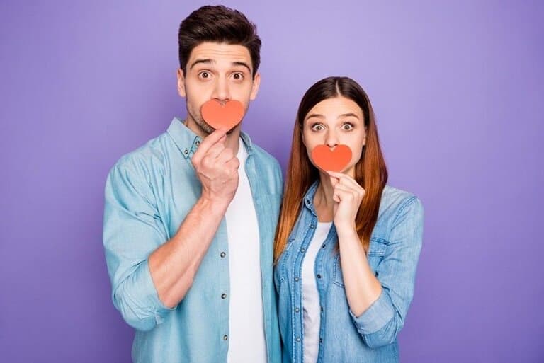 Casal segurando corações de papel diante da boca