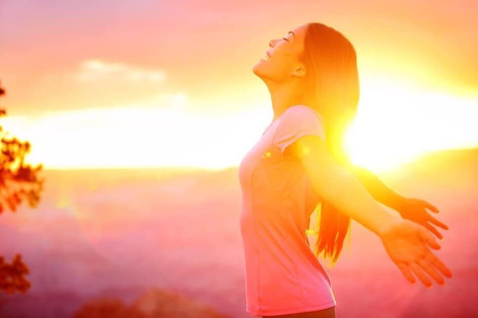 Mulher de olhos fechados e braços abertos sob a luz do pôr do sol