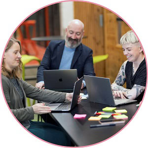 Circle image of people sat around a table with laptops and postit notes