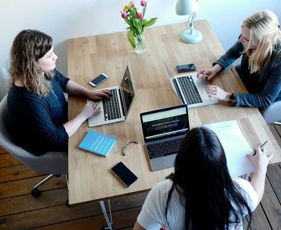 Three people sat around a table with laptops