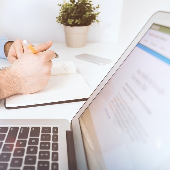 Laptop and person writing in a notepad